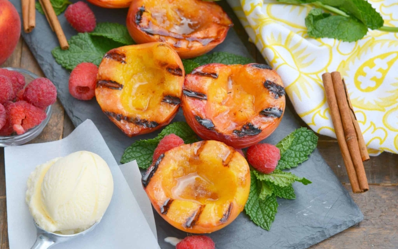 Grilled Peaches basted with cinnamon brown sugar and butter are the ultimate summer dessert idea. Add vanilla ice cream and fresh raspberries for dessert perfection! #grilledpeaches www.savoryexperiments.com