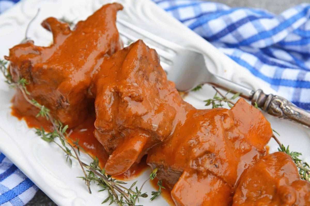 several short ribs covered in sauce on a white serving plate with thyme 