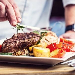 hand garnishing steak with fresh herbs