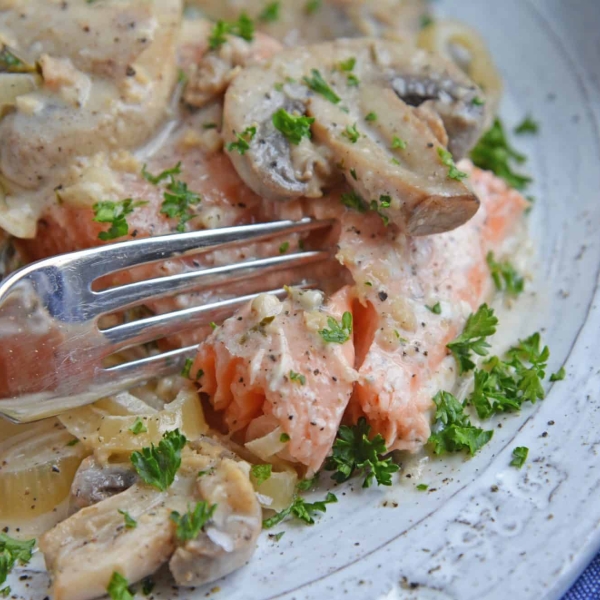 Fork cutting into a salmon fillet in asiago mushroom sauce