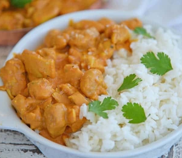 A bowl of rice on a plate, with Butter and Chicken