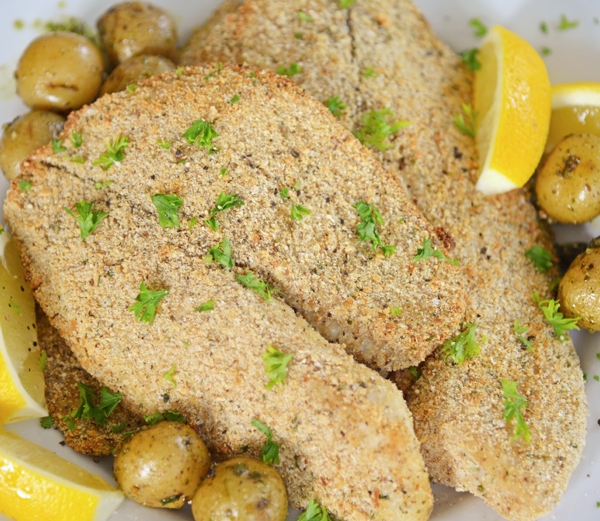 A plate of breaded tilapia with lemons and parsley