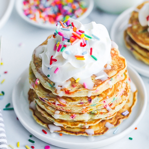 angle view of a stack of funfetti pancakes topped with whipped cream and sprinkles