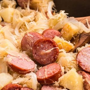 close up of wooden spoon in skillet of sauerkraut and pork