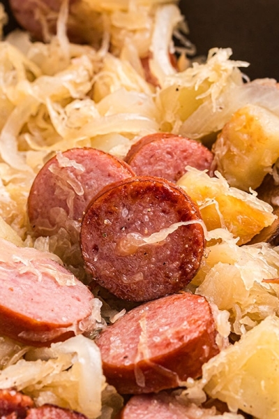 close up of wooden spoon in skillet of sauerkraut and pork