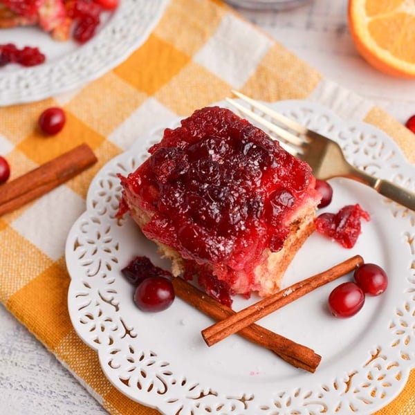 angled shot of cranberry cinnamon roll on plate with fork and cinnamon sticks