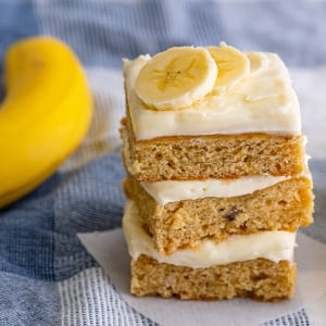 stack of frosted banana blondies with fresh banana slices on top