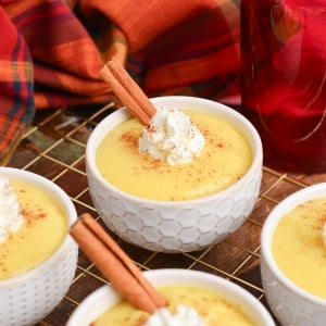 angled shot of bowls of eggnog pudding with whipped cream and cinnamon sticks on wire rack