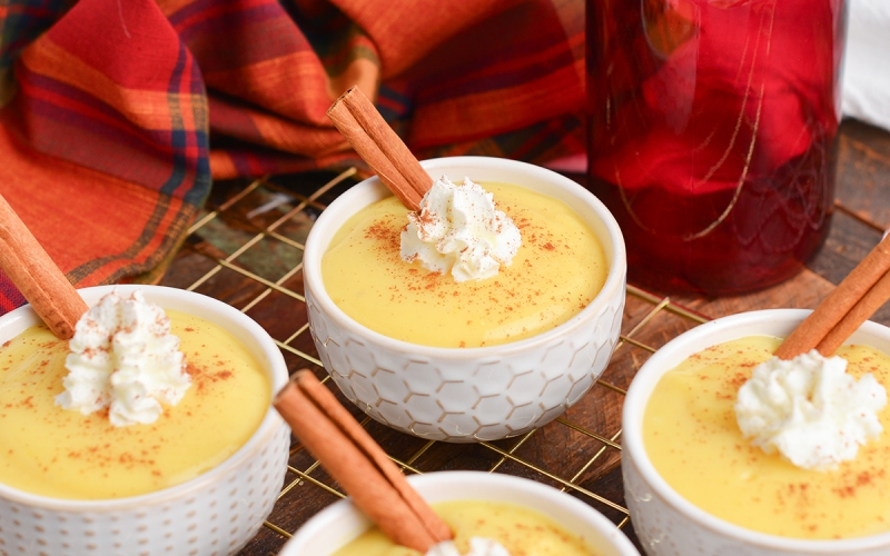 angled shot of bowls of eggnog pudding with whipped cream and cinnamon sticks on wire rack