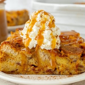 straight on shot of slice of pumpkin bread pudding topped with whipped cream and caramel