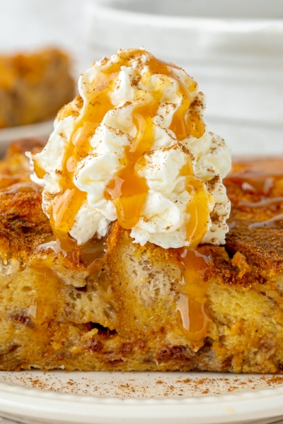 straight on shot of slice of pumpkin bread pudding topped with whipped cream and caramel