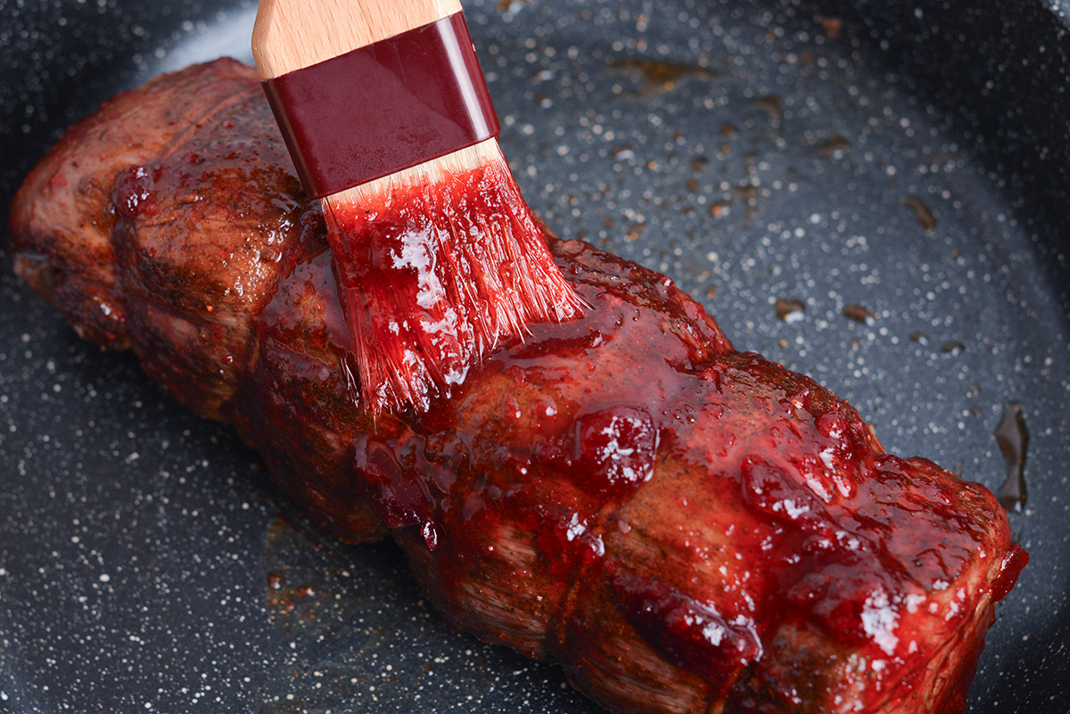 basting brush covering a beef tenderloin with cranberry glaze