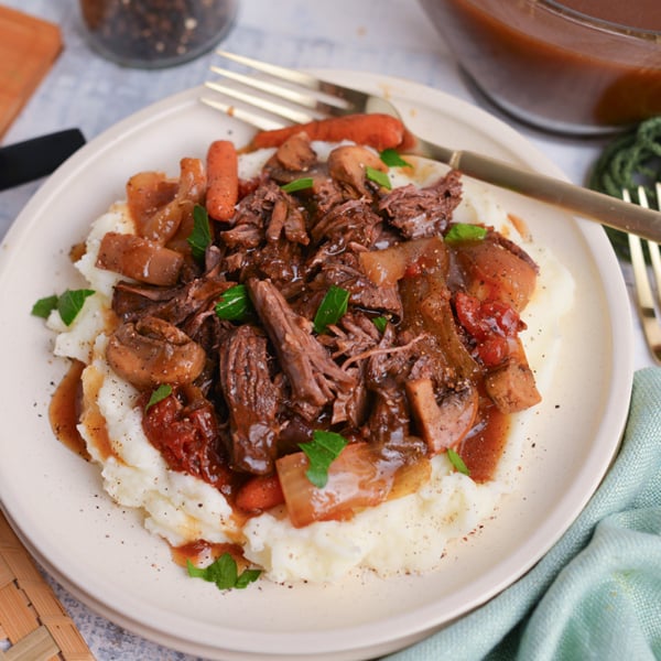 close up angled shot of balsamic pot roast over mased potatoes on plate