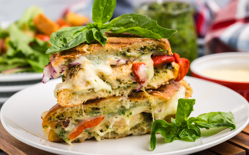 straight on shot of Italian chicken panini halves on plate topped with basil