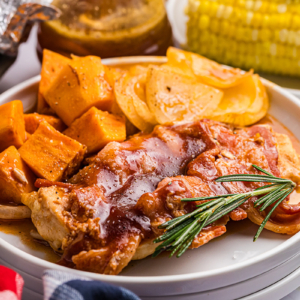 angled shot of bbq chicken and sweet potatoes on plate with rosemary