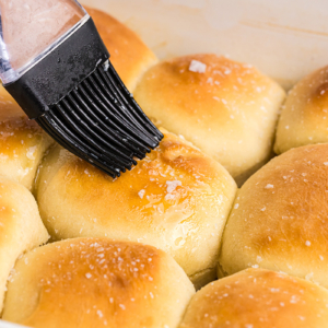 angled shot of butter brushed onto pan of dinner rolls