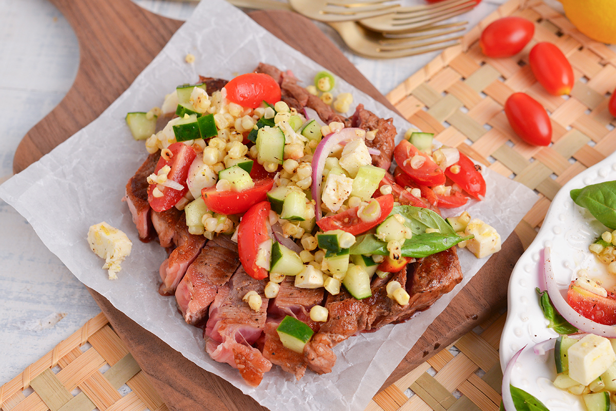 angled shot of corn and tomato salad over steak on a plate