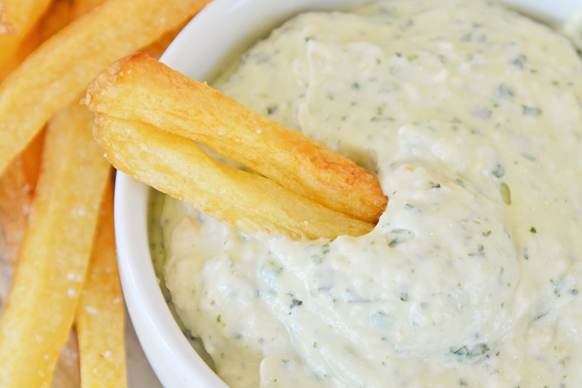 close up of french fries dipping into aioli sauce