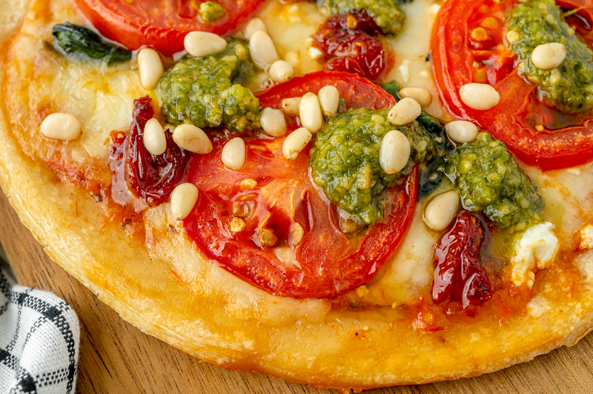 close up shot of tomato pesto pizza on cutting board