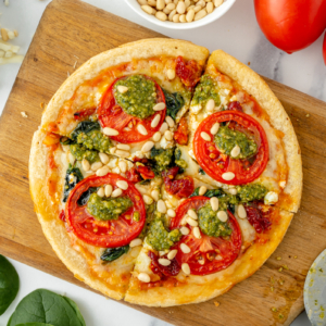 sliced tomato pesto pizza on cutting board