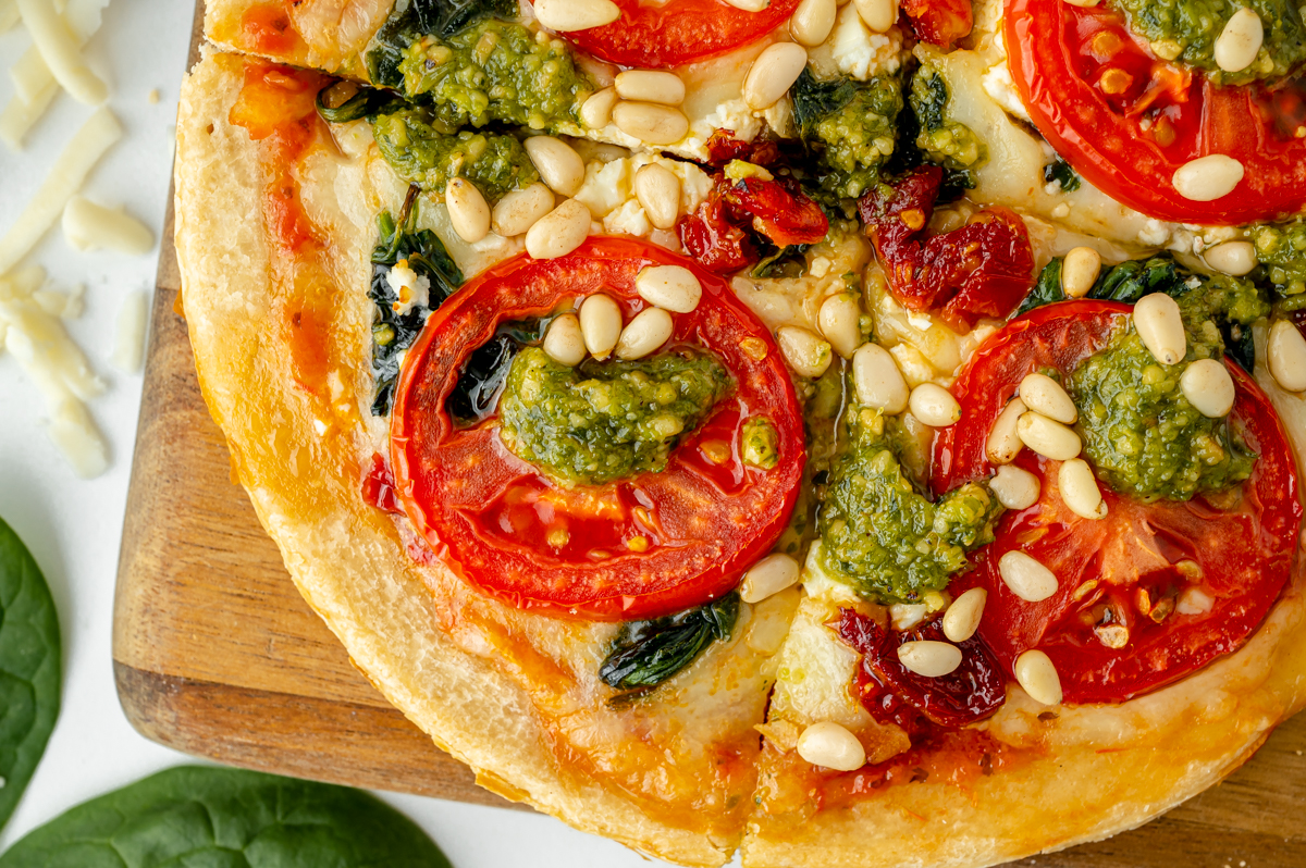 close up shot of sliced tomato pesto pizza on cutting board