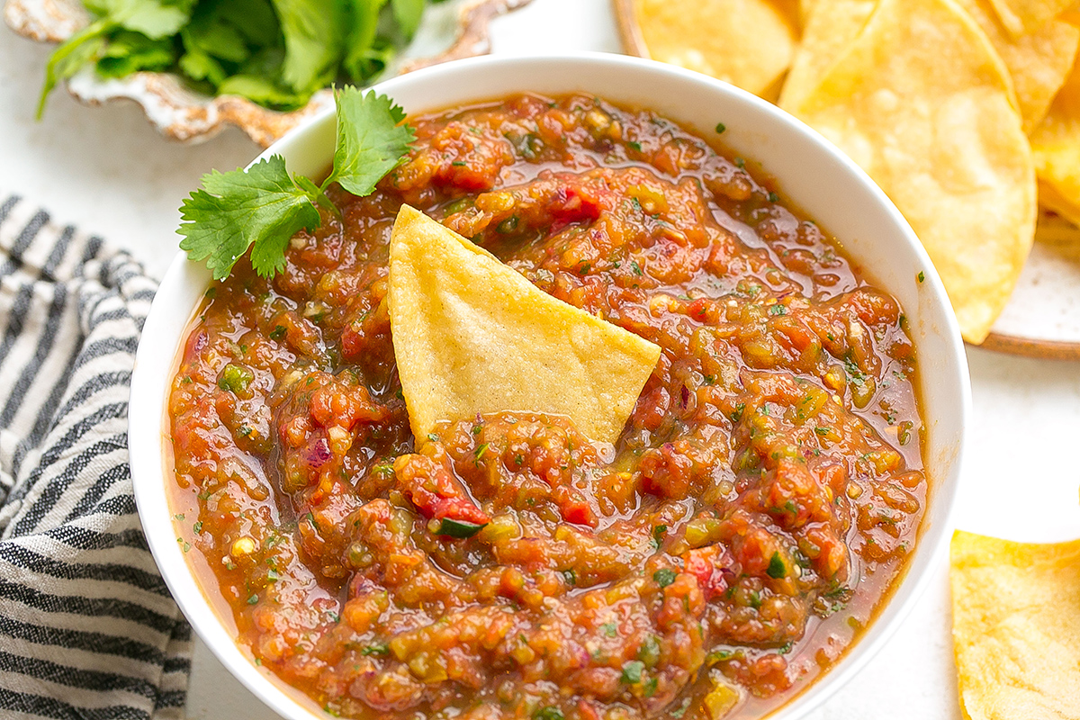 close up angled shot of tortilla chip in bowl of blender salsa