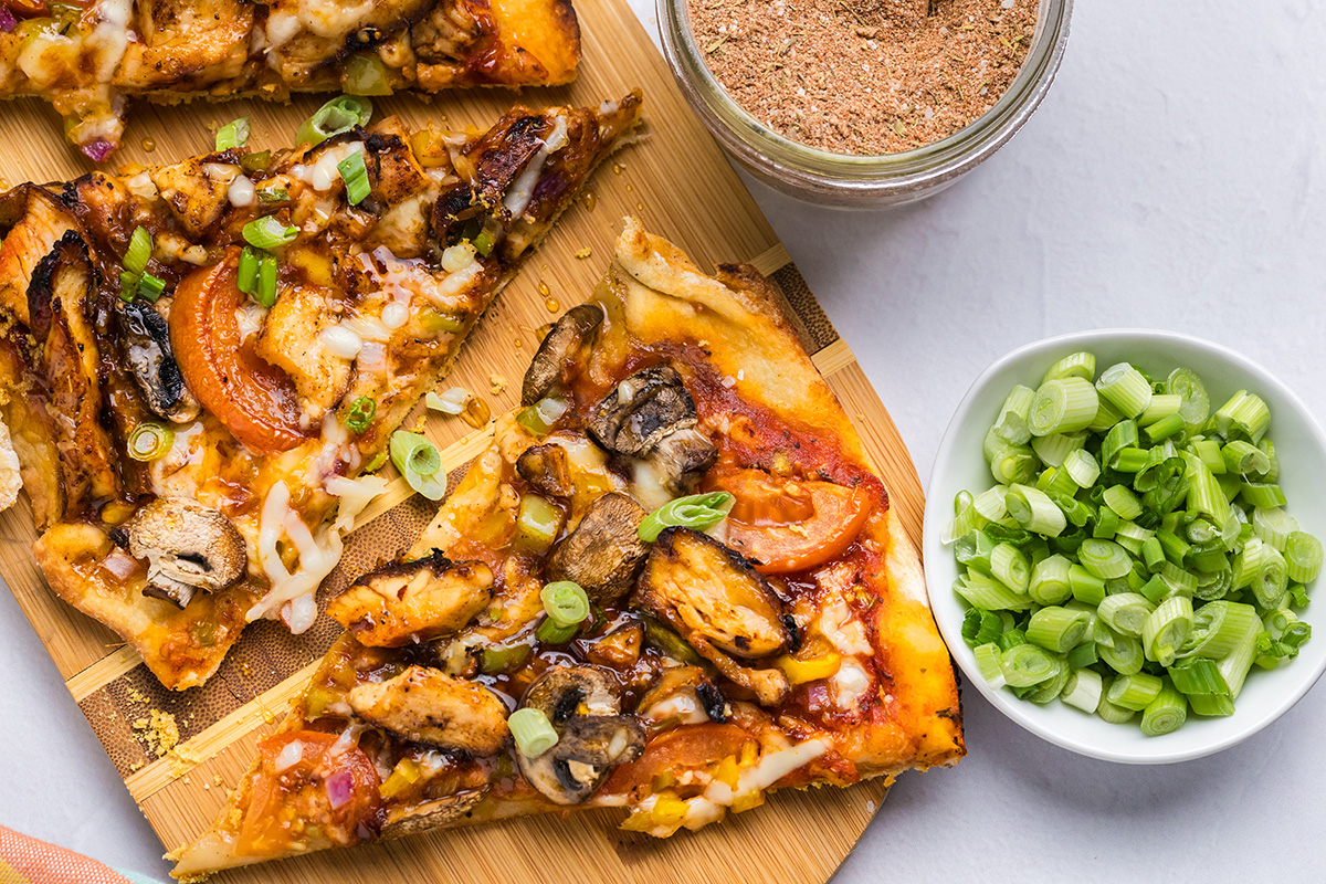 overhead shot of slices of caribbean pizza with bowl of scallions