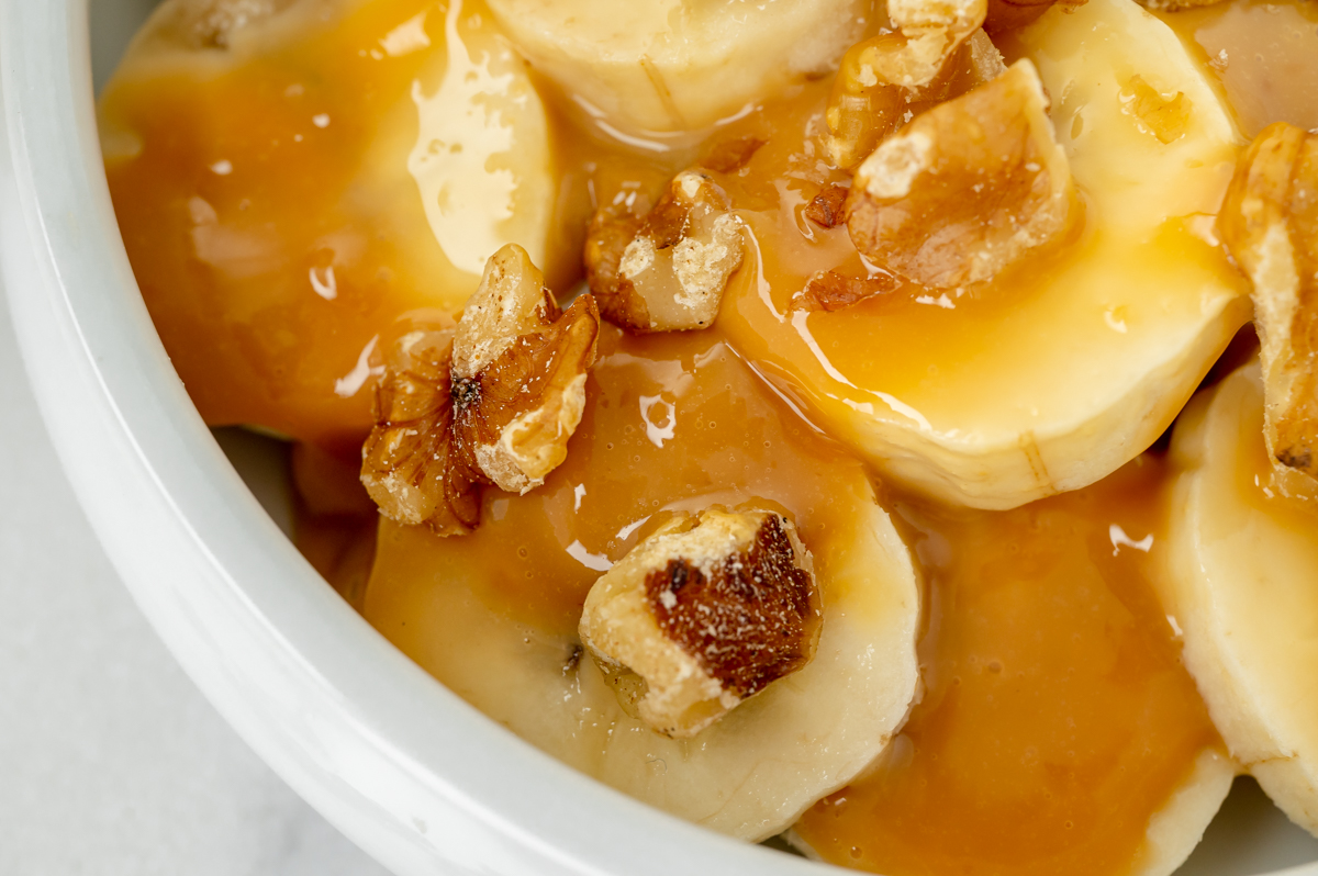 overhead shot of sweetened condensed milk caramel over sliced bananas and walnuts