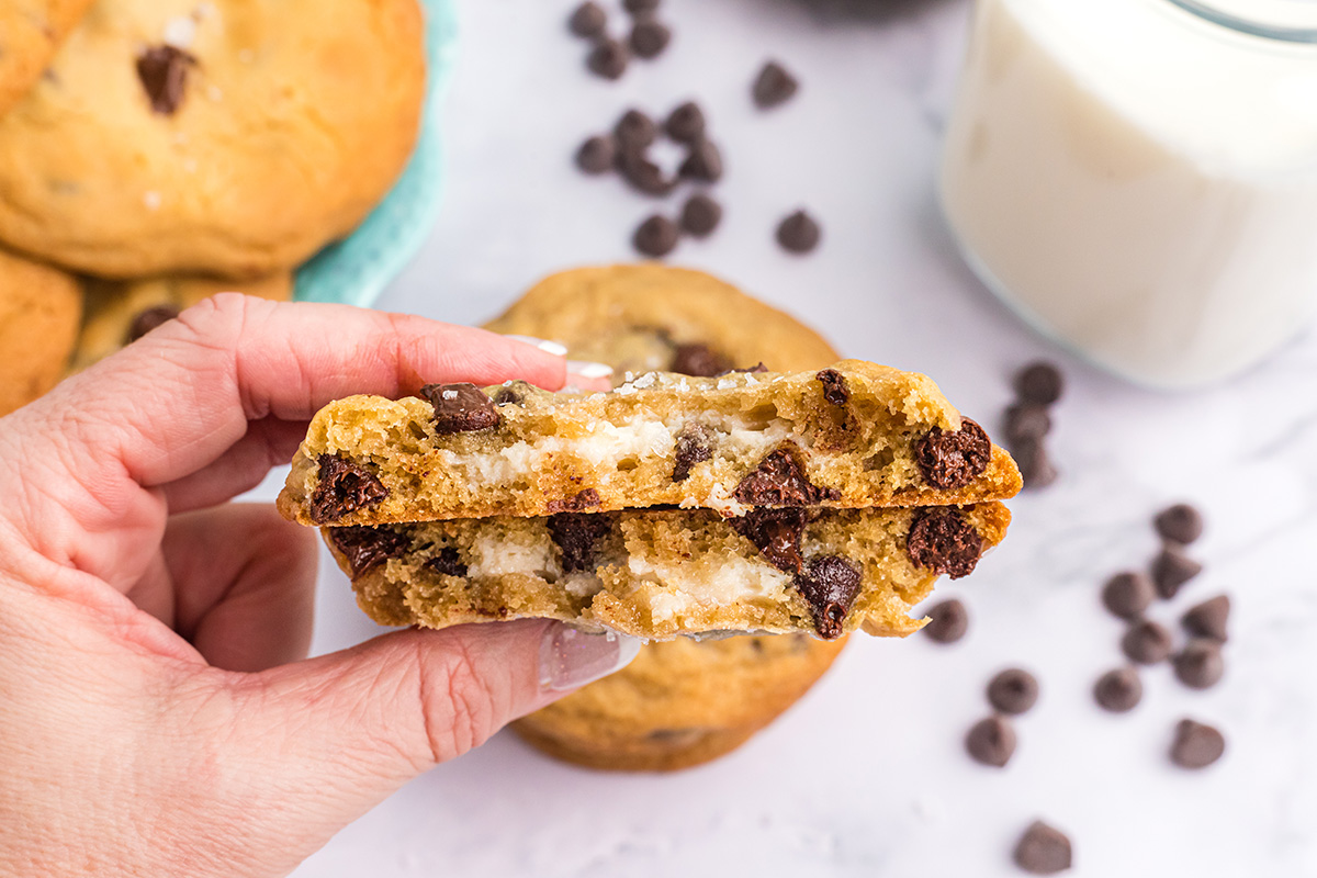 hand holding a chocolate chip cookie stuffed with cream broken in half 