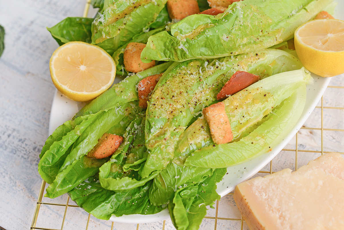 angle close up view of lettuce leaves with garlic dressing, croutons and fresh lemons