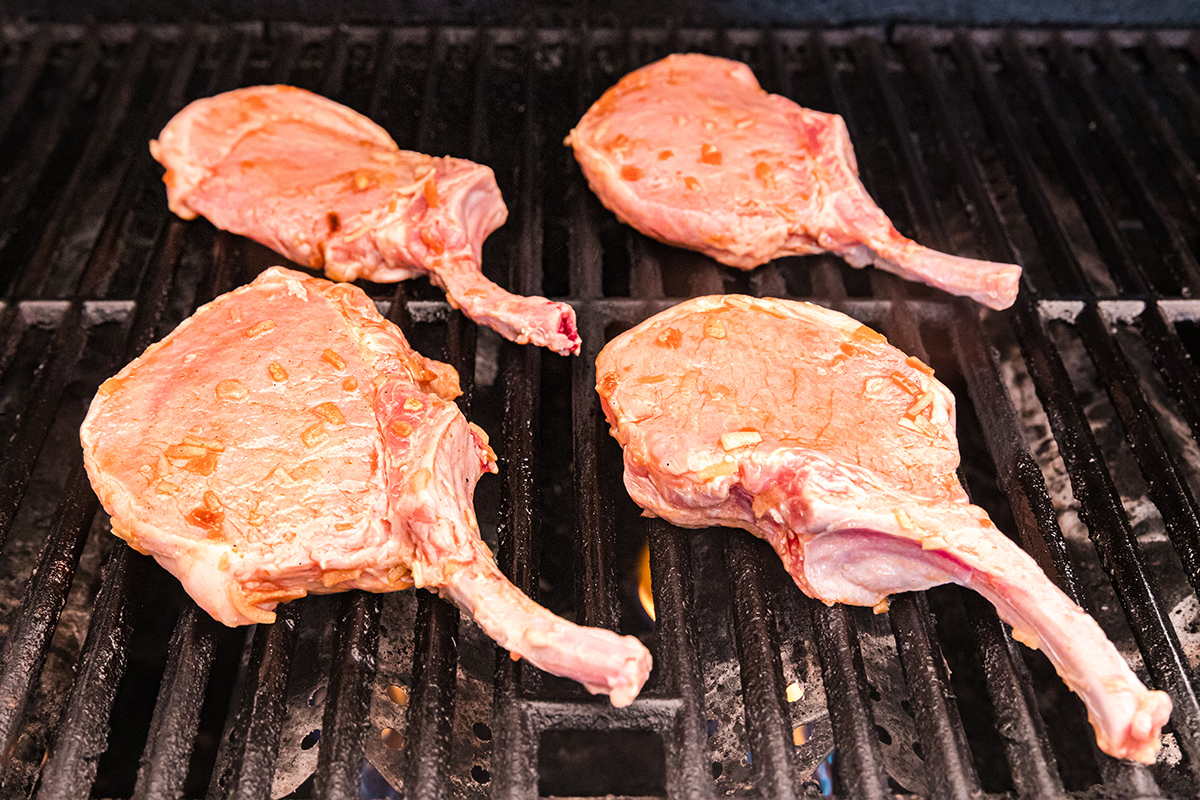 angled shot of raw pork chops cooking on grill