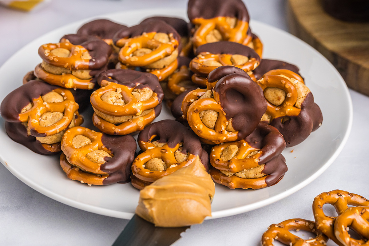 angled shot of peanut butter pretzel bites on plate with knife of peanut butter