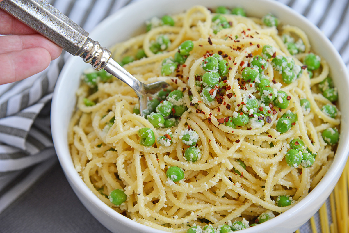 fork digging into pasta and peas in a white bowl