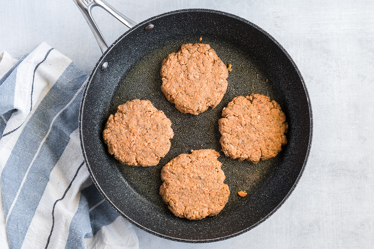 overhead shot of four salmon burgers cooking in skillet