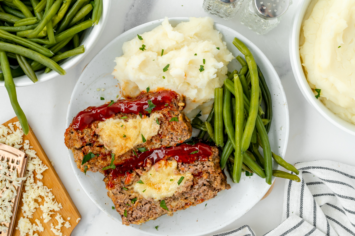 overhead shot of two slices of stuffed meatloaf on plate with potatoes and green beans