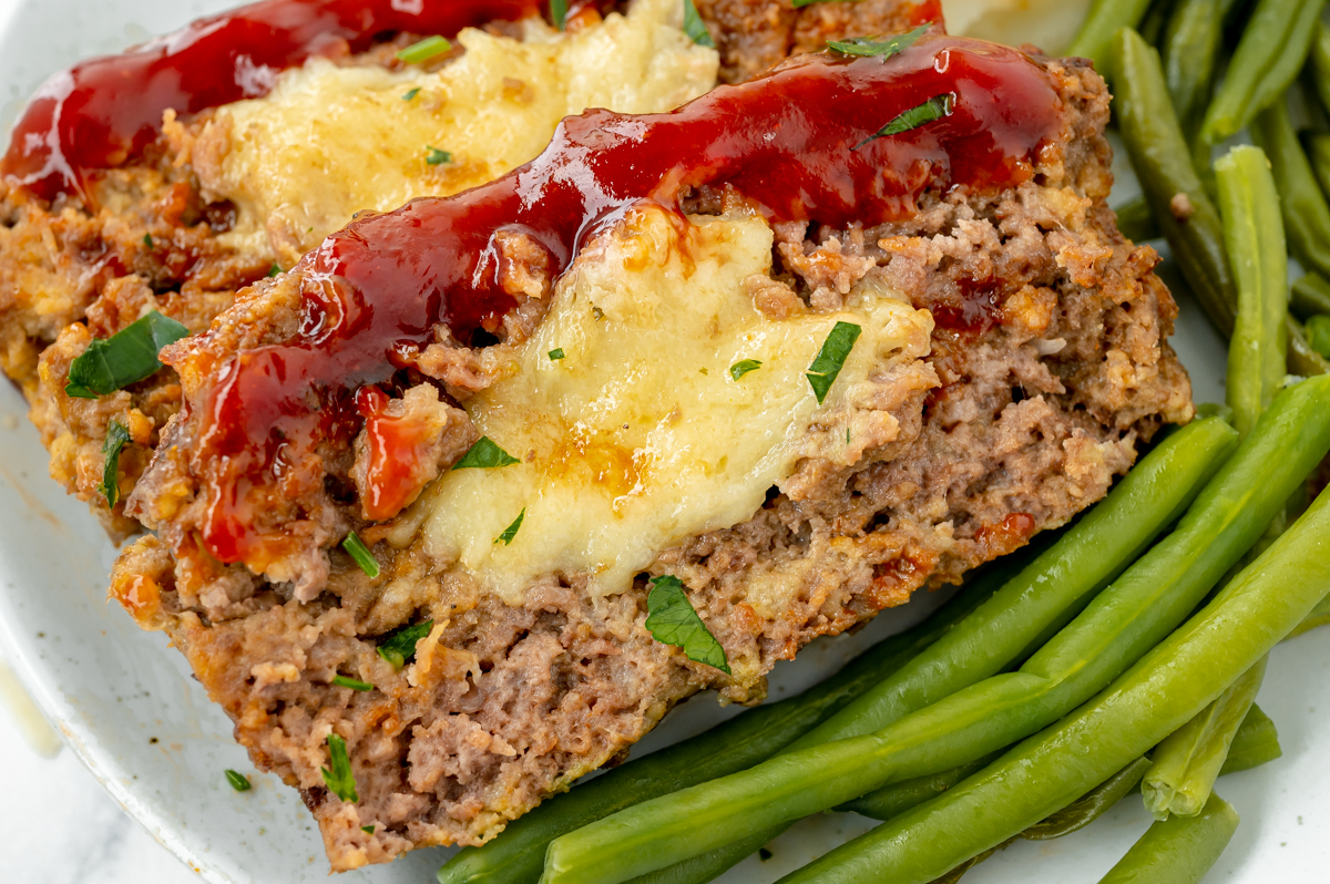 close up angled shot of sliced stuffed meatloaf on plate with green beans