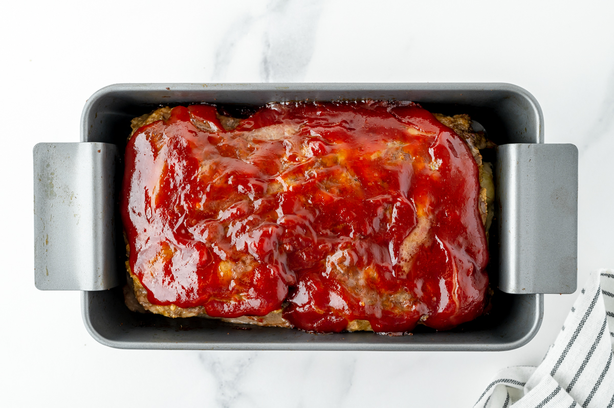 overhead shot of glaze added to top of cooked meatloaf in pan