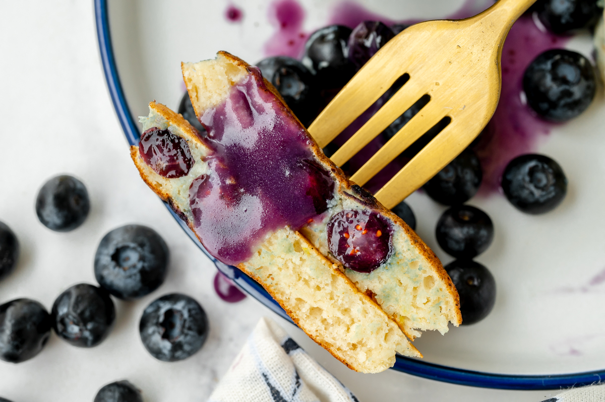 overhead shot of bite of pancakes topped with blueberry syrup on fork