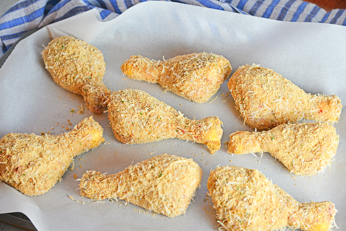 breaded chicken drumsticks on a parchment lined baking sheet