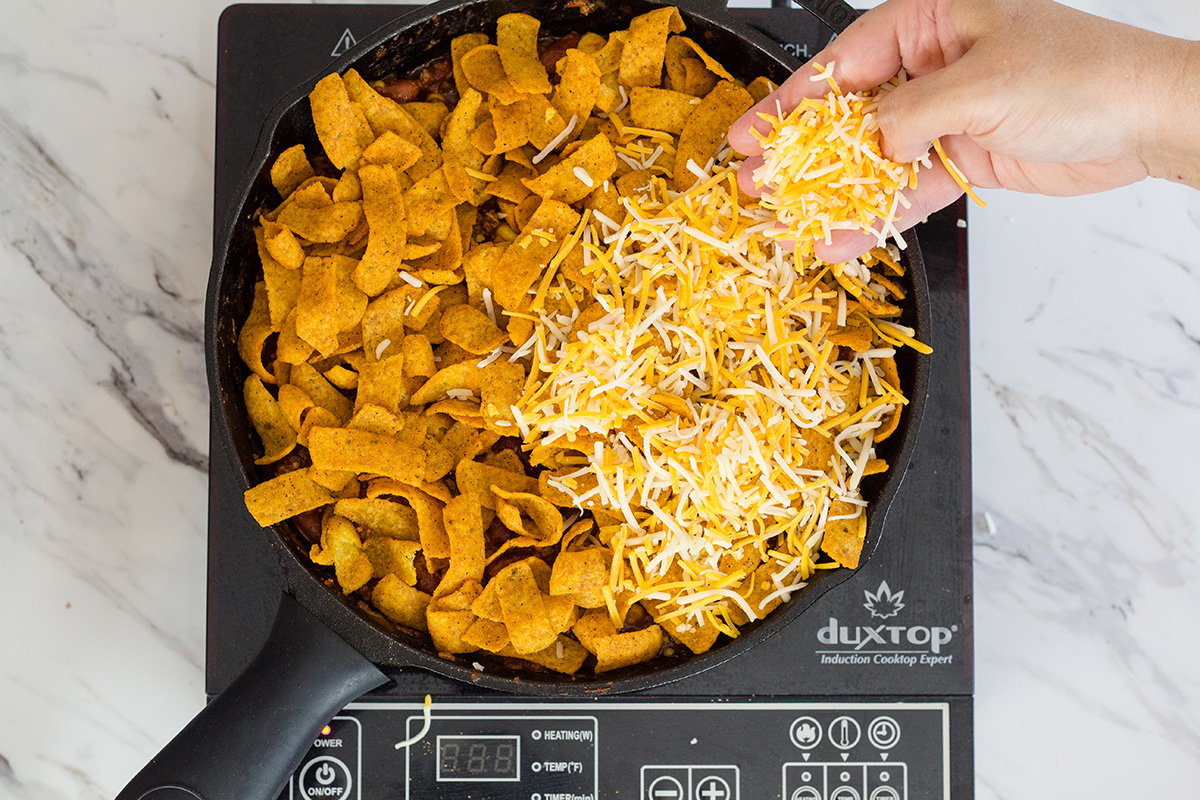 cheese sprinkling over fritos in skillet