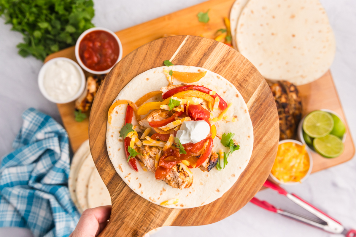 overhead shot of hand holding board of chicken fajita