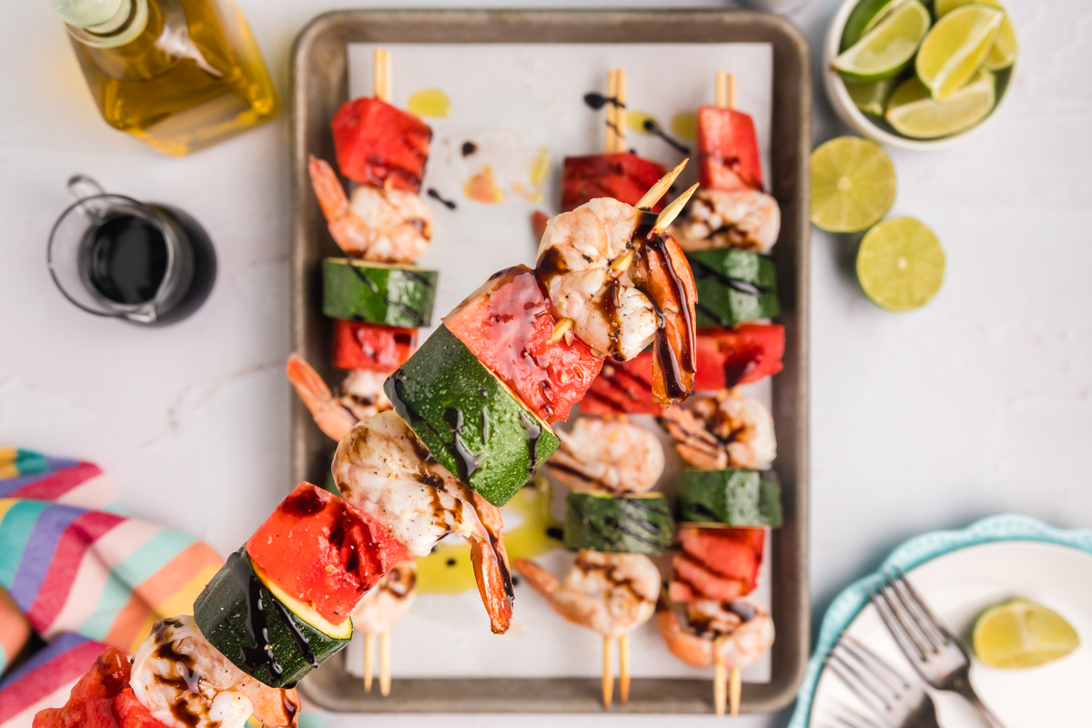 hand holding watermelon shrimp kabob over sheet pan of kabobs