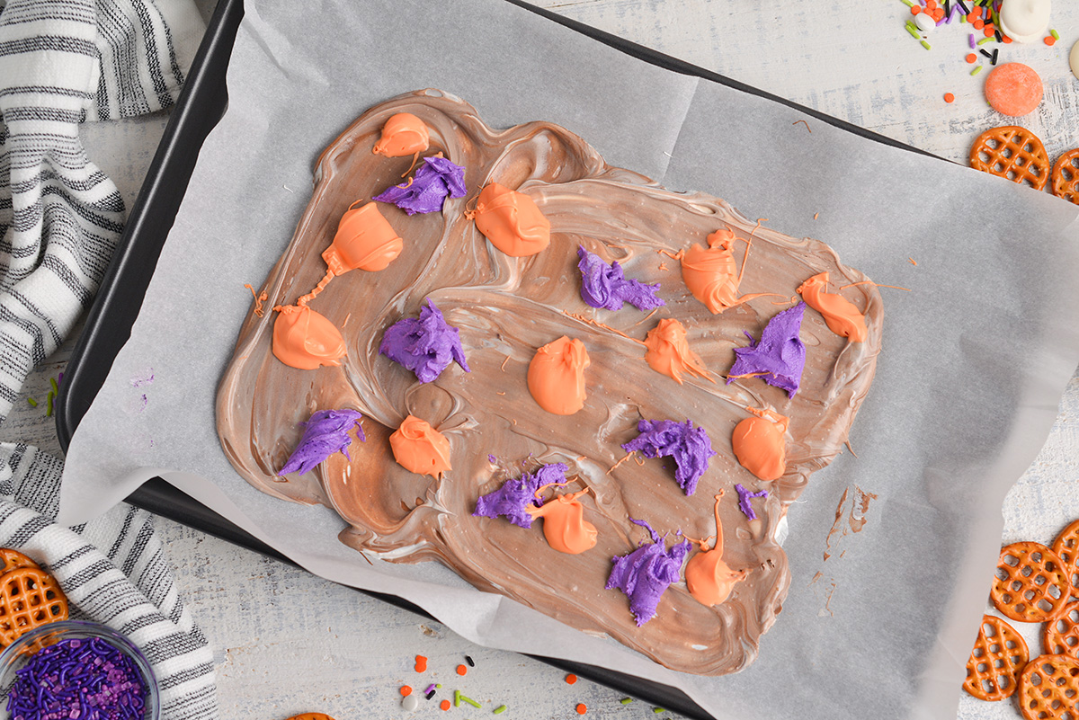 colored chocolate spooned over melted chocolate on sheet pan