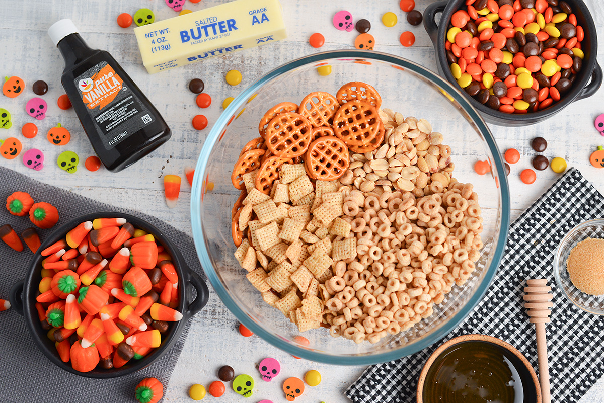 ingredients for halloween snack mix including peanuts, pretzels, chex mix, cheerios and candy coating mix