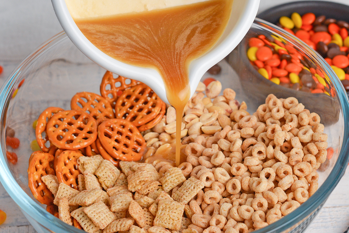 pouring honey butter mixture over a snack mix