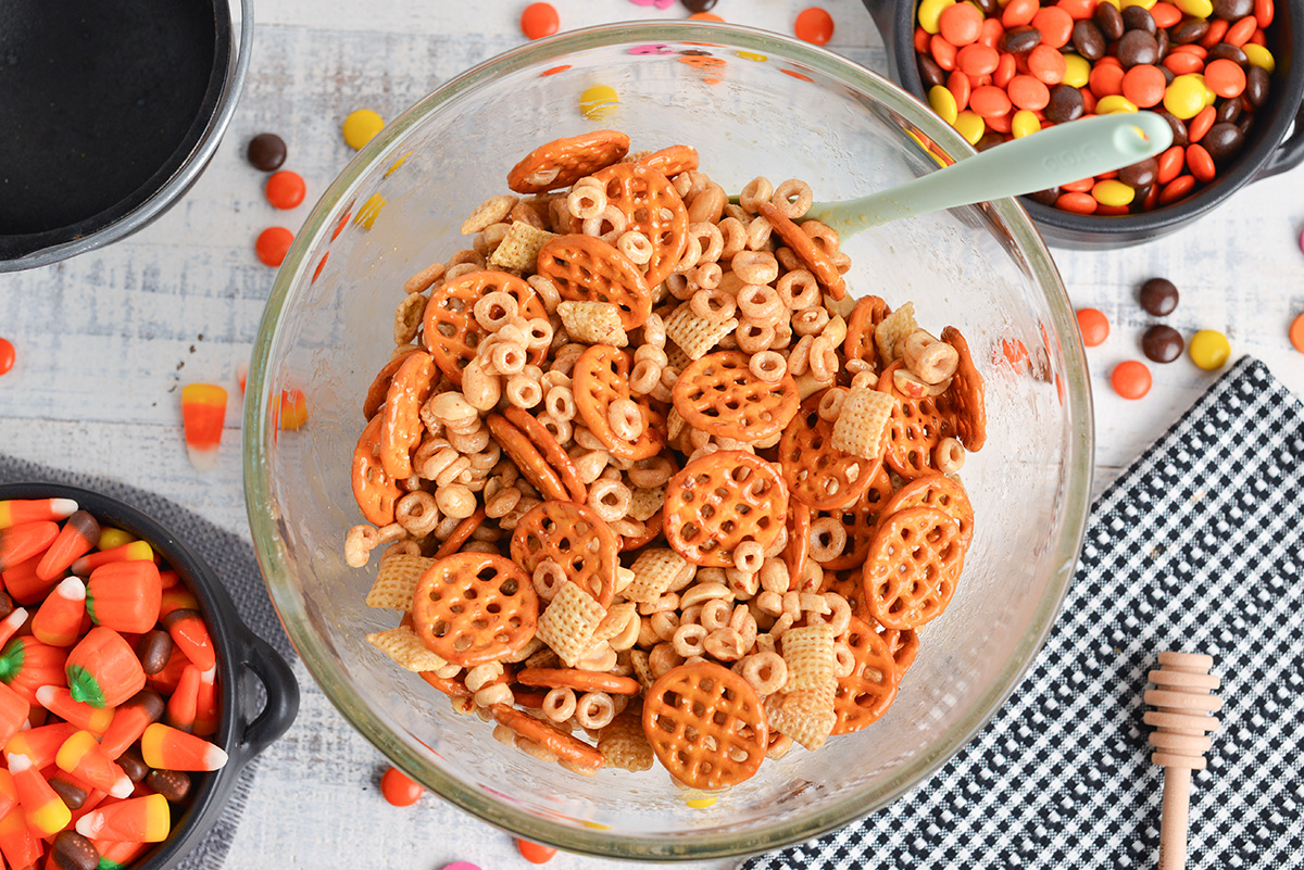 snack mix ingredients tossed in honey nut candy coating in a large mixing bowl