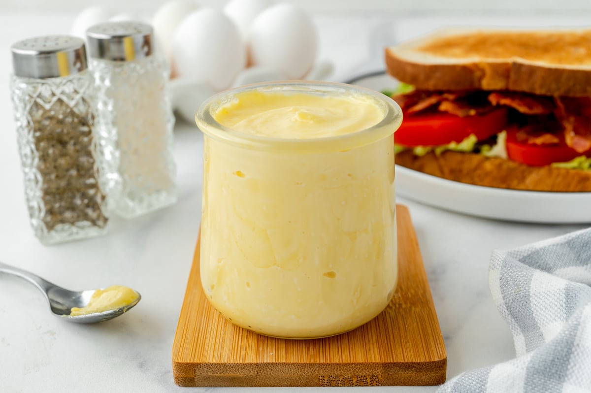 angled shot of jar of homemade mayonnaise on wooden board