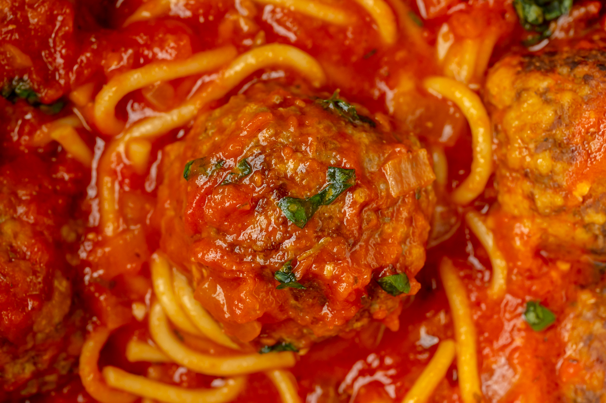 close up overhead shot of meatball in sauce with spaghetti