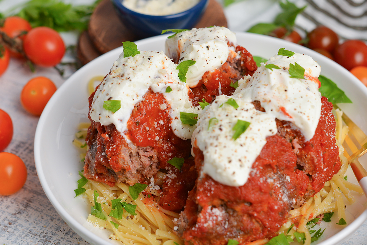 close up angled shot of lavo one pound meatball cut into fourths over pasta