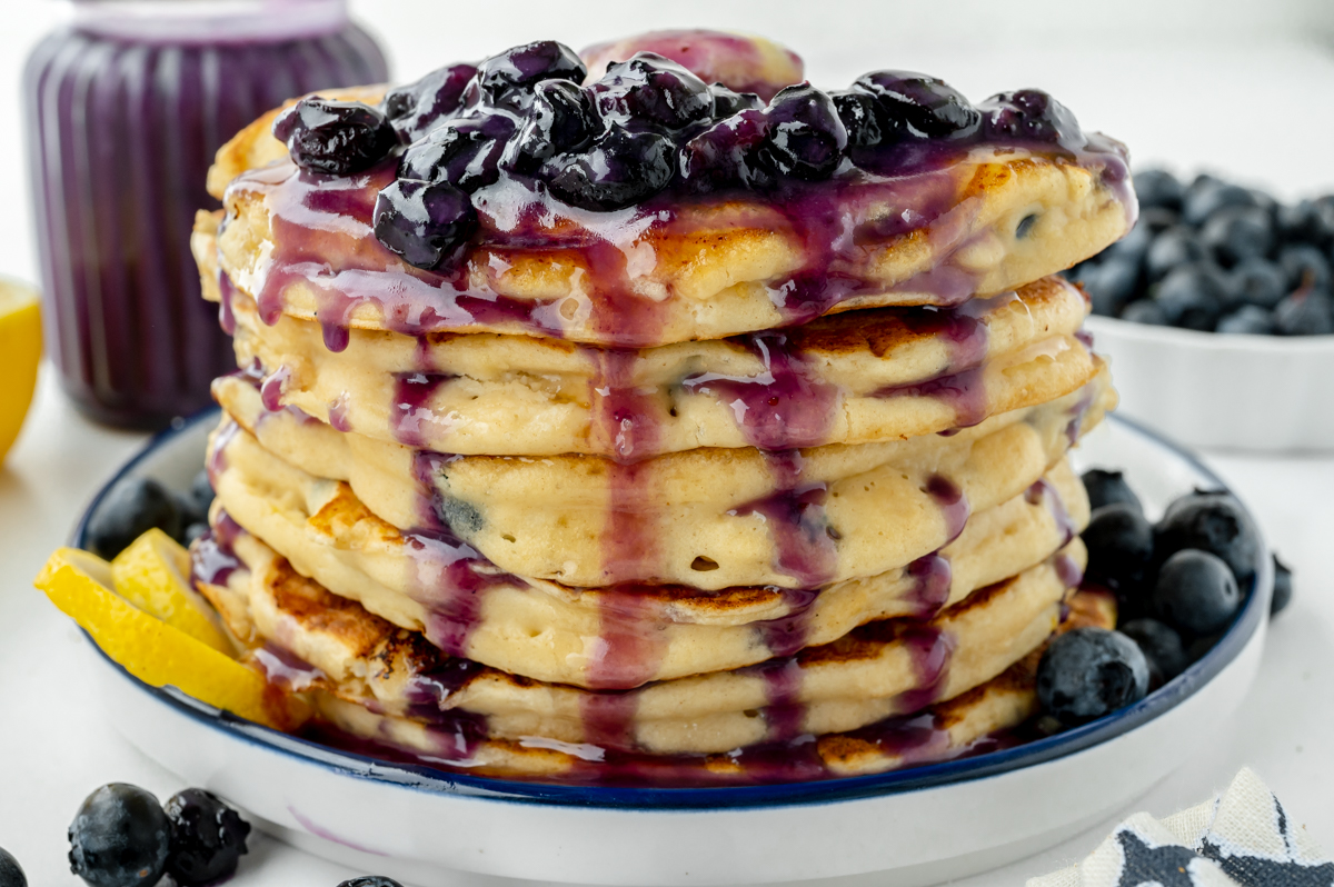 angled shot of stack of pancakes topped with blueberry syrup